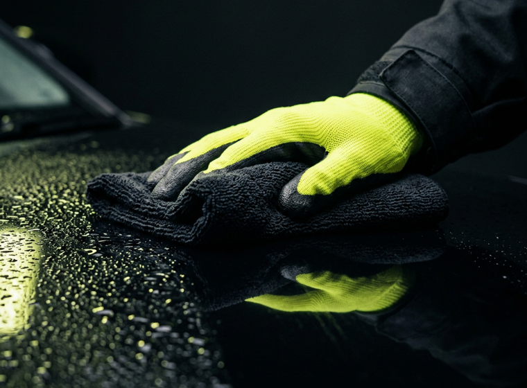 Close-up van een Clean Patrol-medewerker die een donker oppervlak streeploos afneemt met een microvezeldoek